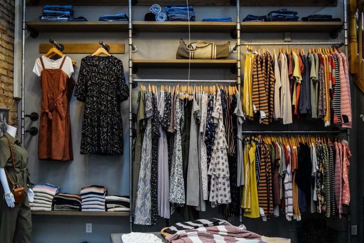 Interior de tienda fast fashion con racks de ropa en colores neutros y básicos colgados en serie, idéntica oferta entre marcas